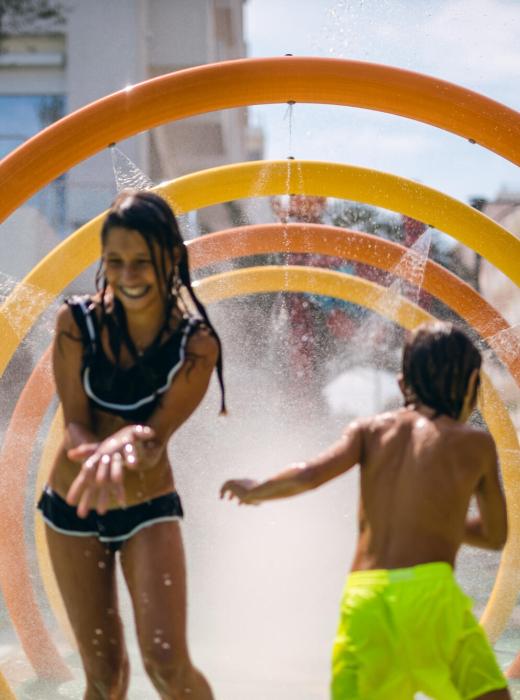 Bambini giocano sotto gli spruzzi d'acqua in un'area giochi all'aperto.