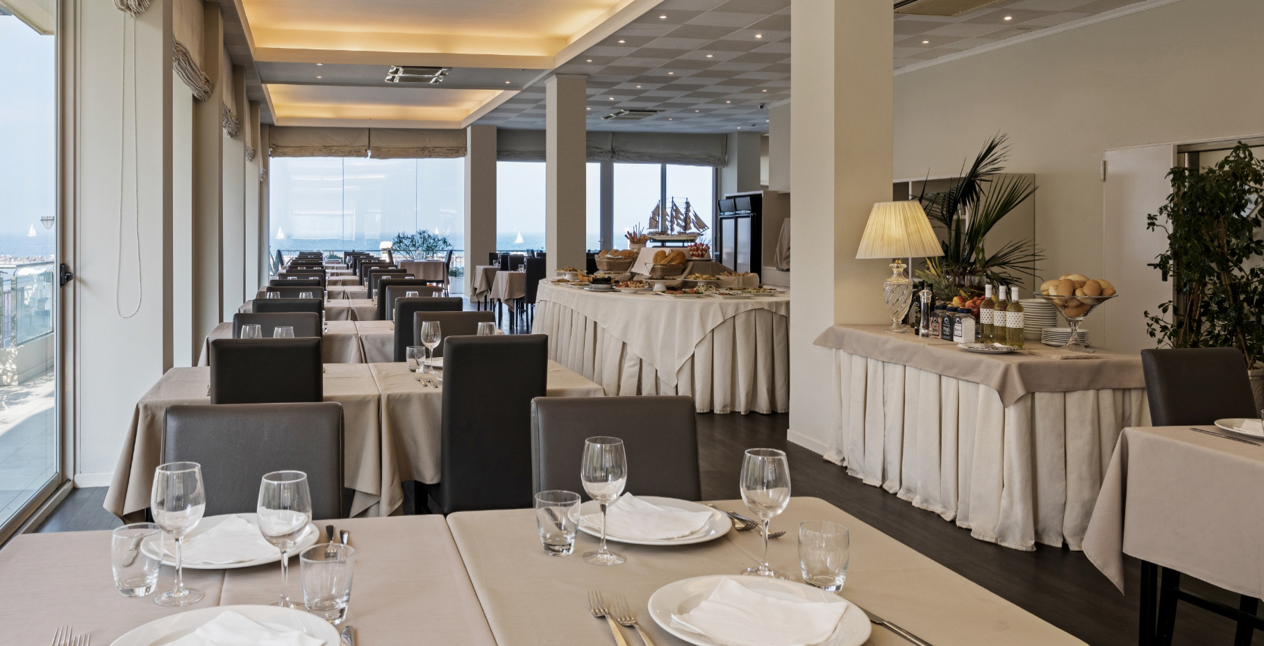 Ristorante elegante con tavoli apparecchiati, vista sul mare e buffet ricco.