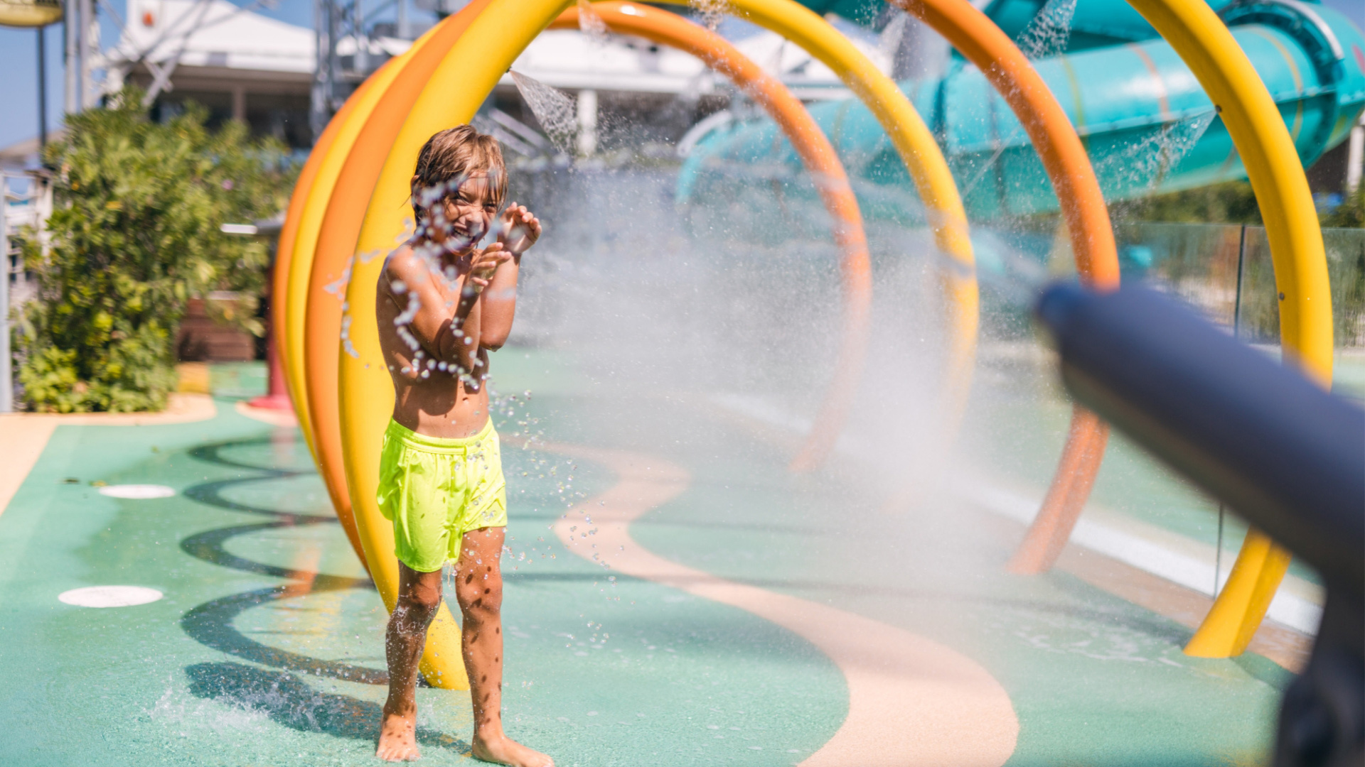 Bambino gioca felice sotto gli spruzzi d'acqua in un parco acquatico.