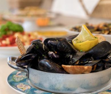 Cozze al vapore con limone e crostini, servite in pentola su piatto decorato.