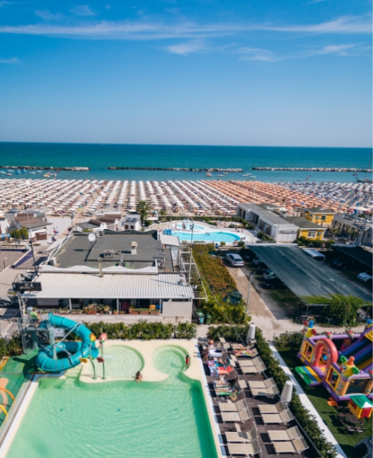 Vista di una spiaggia affollata con piscine e ombrelloni lungo la costa.