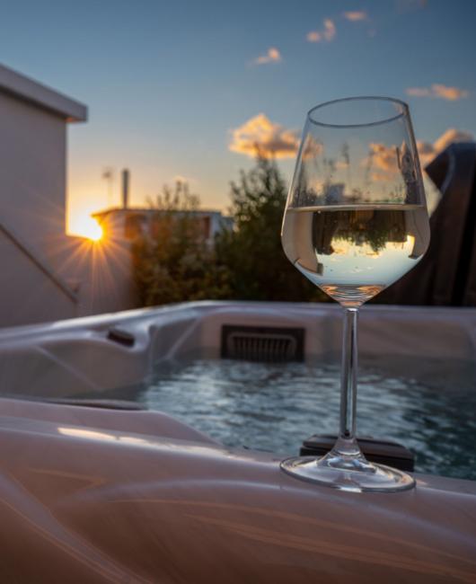 Calice di vino bianco su jacuzzi al tramonto, atmosfera rilassante.