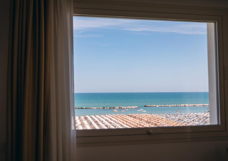 Vista sul mare con ombrelloni dalla finestra di una stanza.