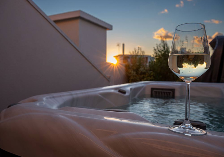 Calice di vino bianco su jacuzzi al tramonto, atmosfera rilassante.