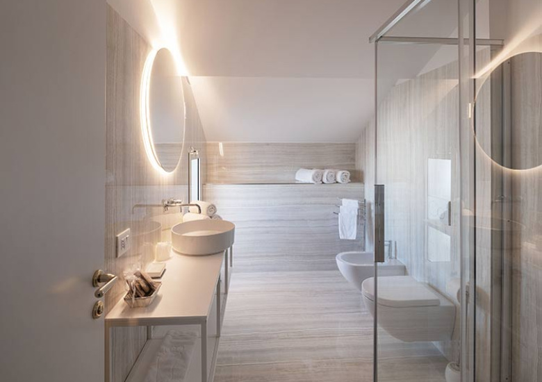 Bagno moderno con lavabo sospeso, doccia in vetro e specchio illuminato.