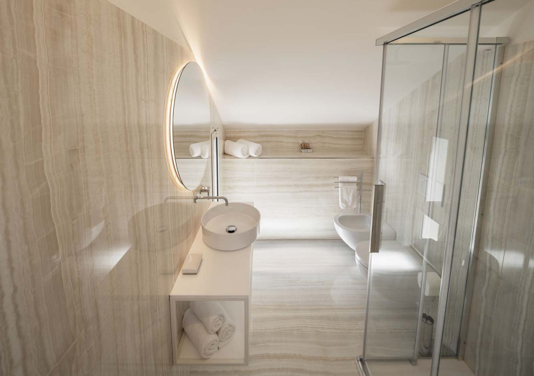 Bagno moderno con lavabo sospeso, doccia in vetro e pareti in marmo chiaro.